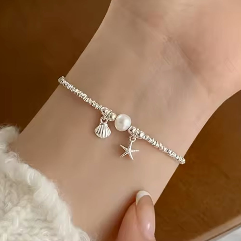 Zierliches Silberarmband mit Perle, Seestern- und Muschel-Anhänger - maritimer Damenschmuck, getragen am Handgelenk, perfekt für sommerliche und elegante Looks.