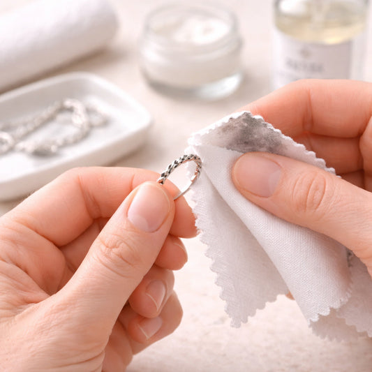 Silberschmuck in Händen mit Reinigungstuch und Pflegeutensilien