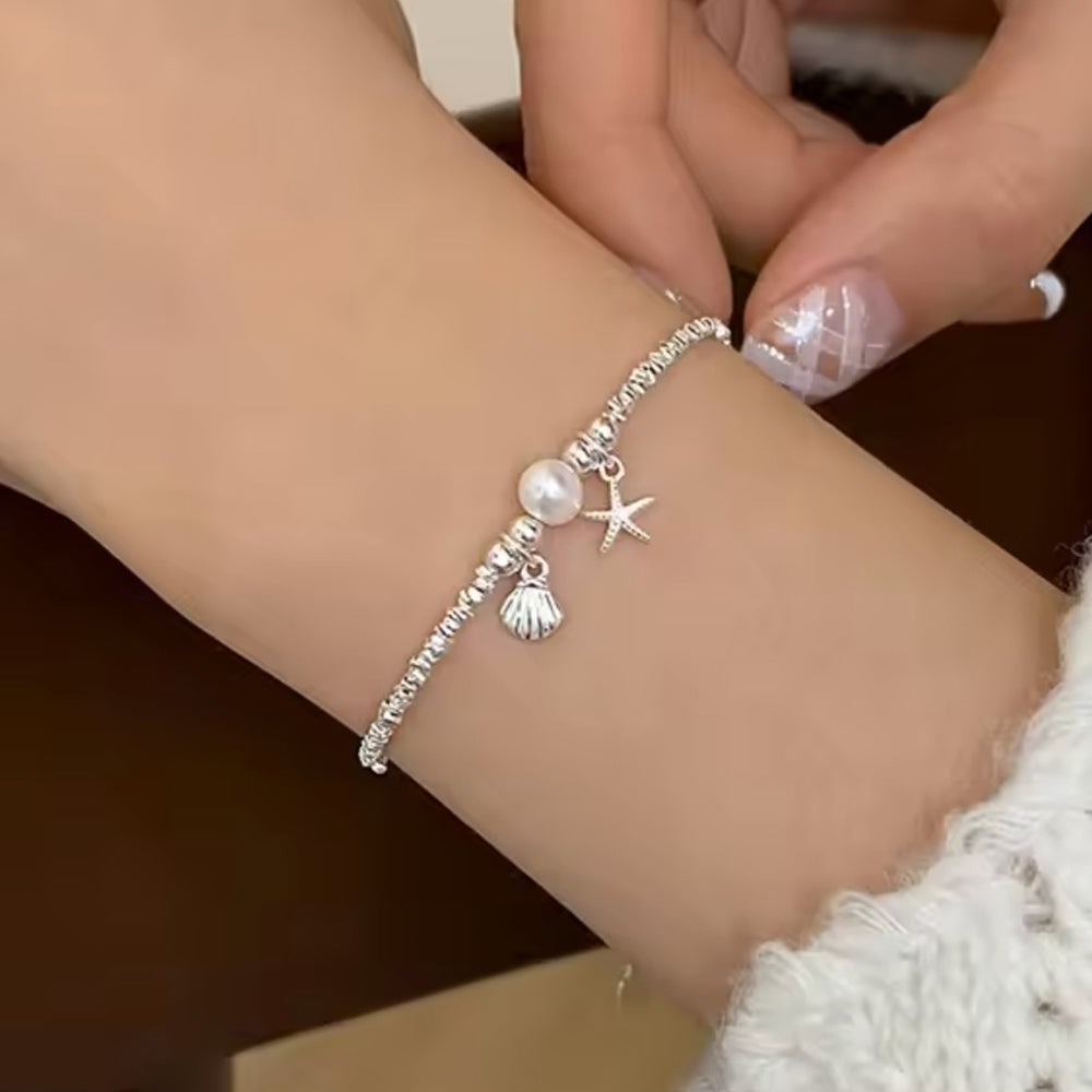 Zierliches Silberarmband mit Perle, Seestern- und Muschel-Anhänger - maritimer Damenschmuck, getragen am Handgelenk, perfekt für sommerliche und elegante Looks.