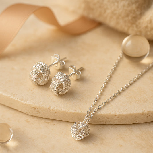 Edles Schmuckset aus silberner Kordelknoten-Kette und passenden Ohrsteckern auf beigem Hintergrund - eleganter Damenschmuck mit zeitlosem Design.